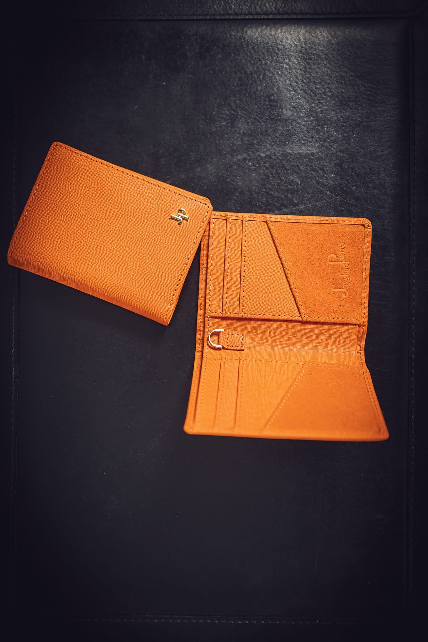 Orange Jayghaer Pierre luxury wallet with gold logo on black leather surface, showcasing inside compartments