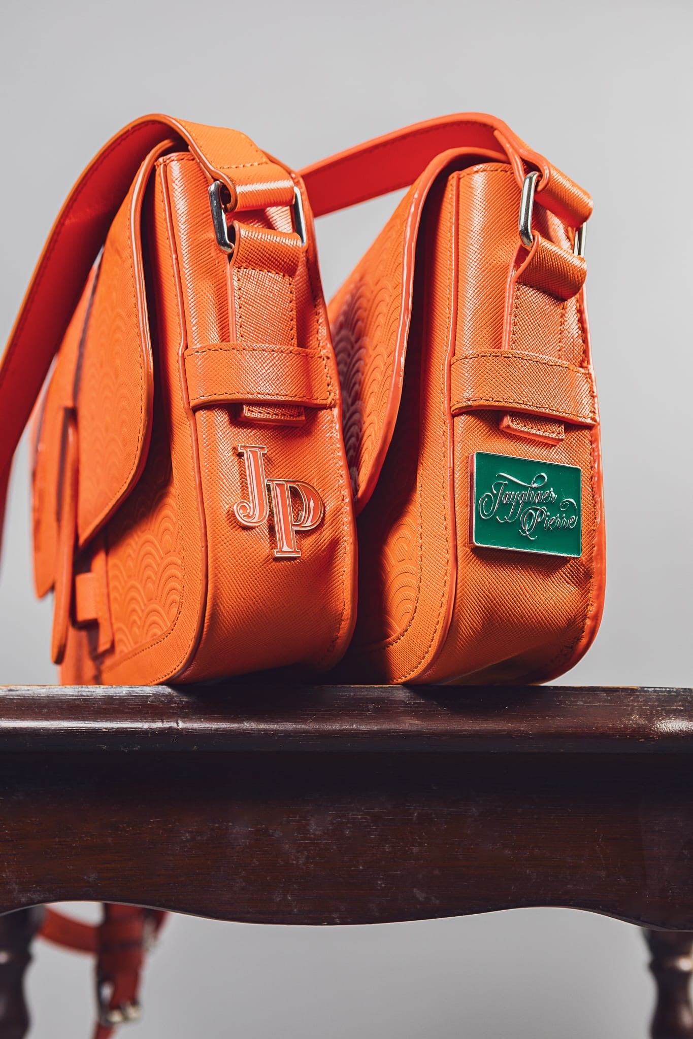 Orange luxury handbag by Jayghaer Pierre with textured pattern and branded metal logos on wooden surface