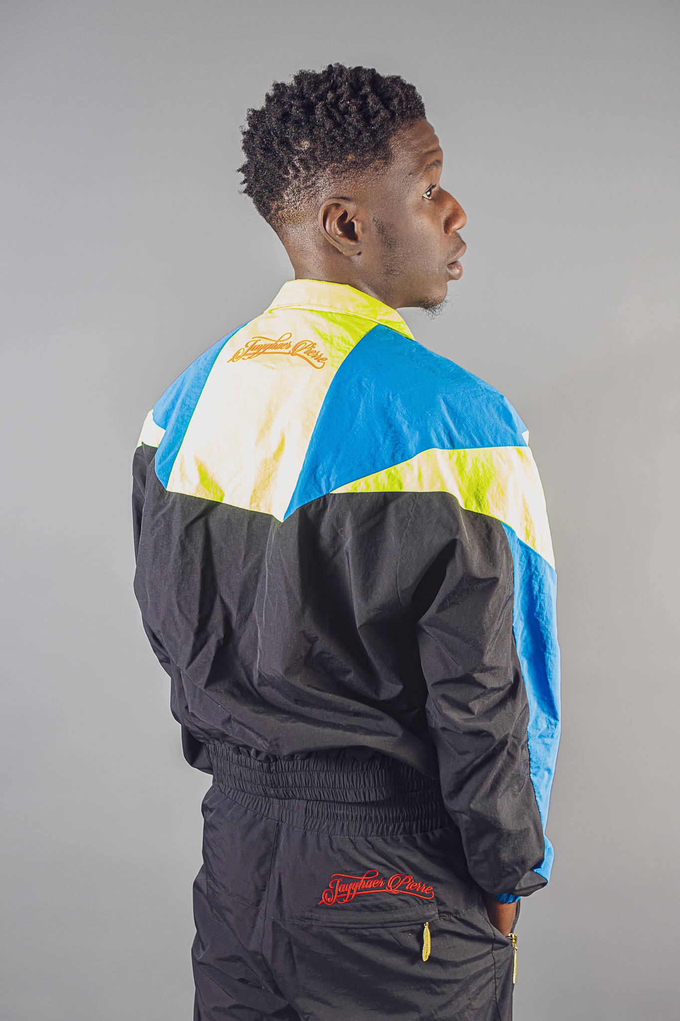 Man wearing Jayghaer Pierre colorblock luxury jacket and pants against gray background