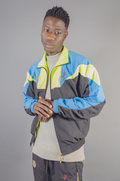 Fashion model wearing JayghaerPierre luxury blue, yellow and black jacket and matching pants against gray background