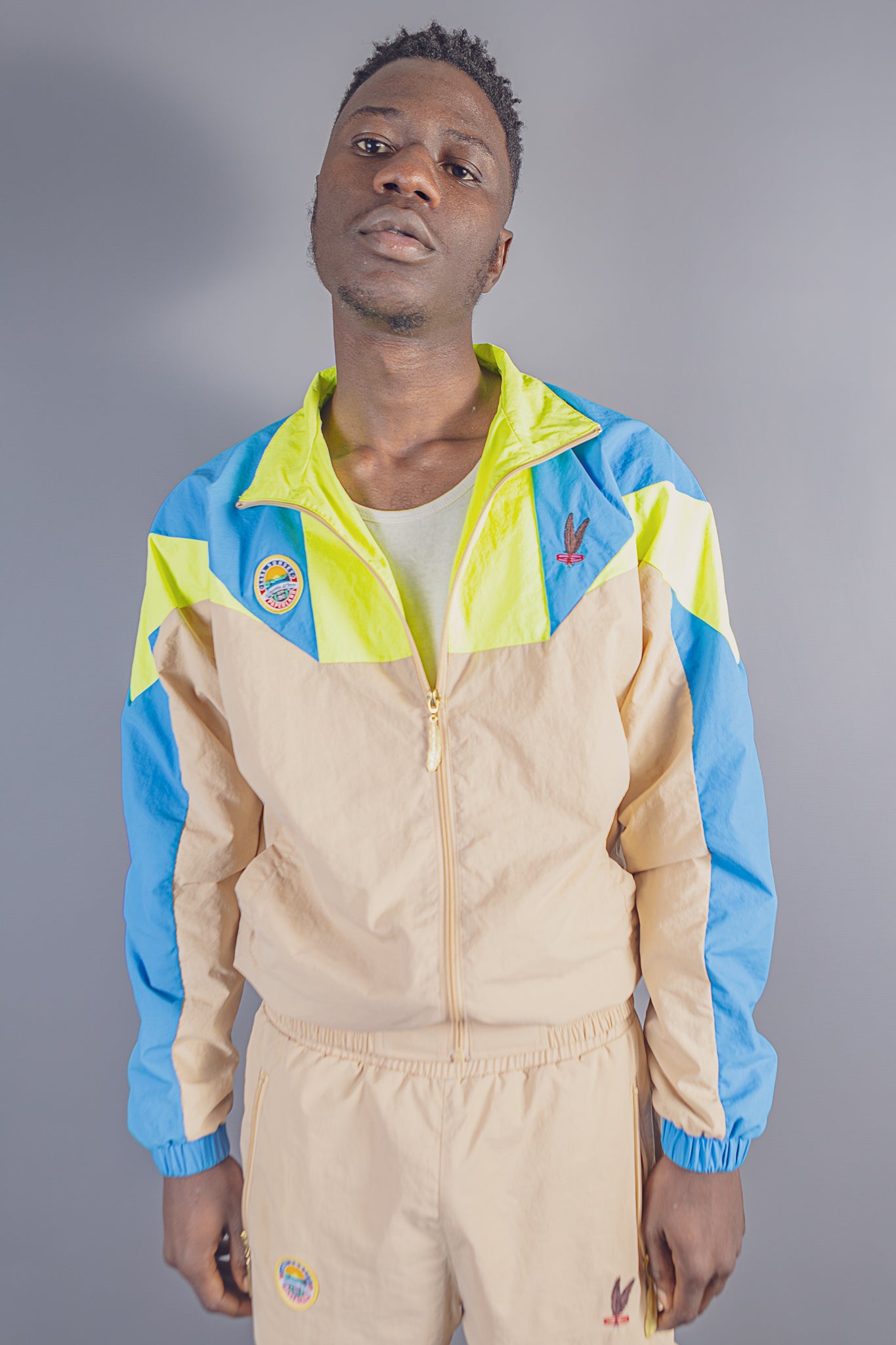 Man wearing Jayghaer Pierre luxury beige tracksuit with blue and neon yellow panels in studio