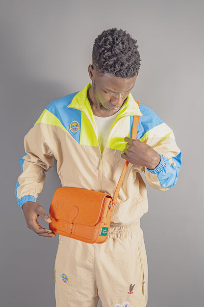 Man wearing beige and blue windbreaker and pants with orange crossbody bag from JayghaerPierre luxury clothing