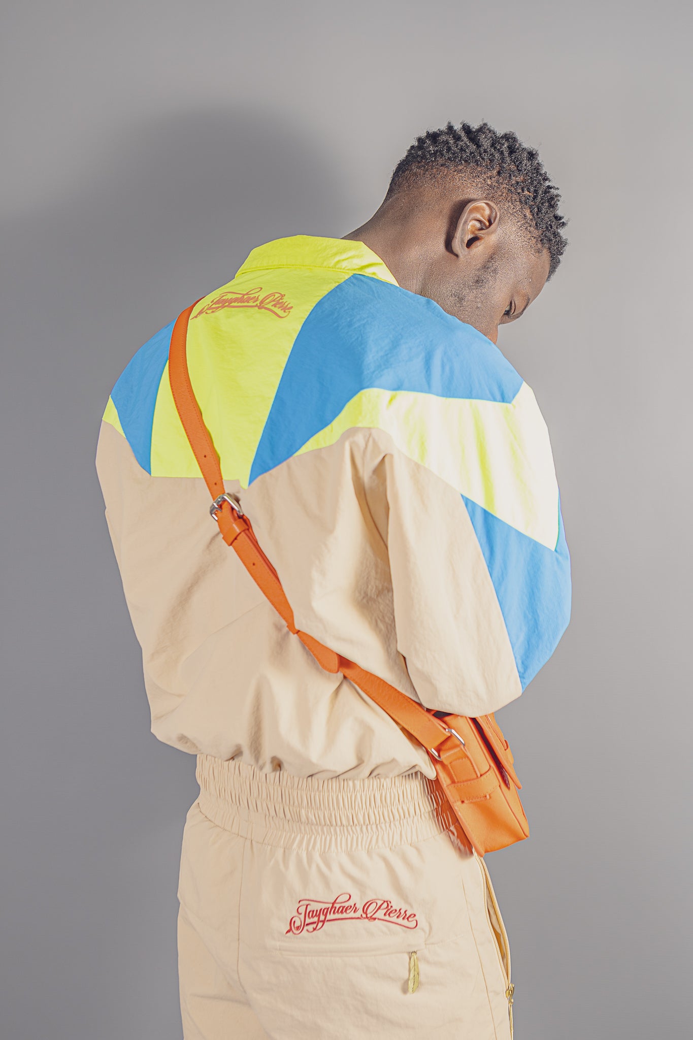 Man wearing Jayghaer Pierre luxury windbreaker with blue, yellow, beige color blocks and orange crossbody bag