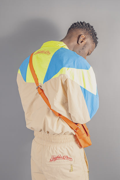 Man wearing Jayghaer Pierre luxury windbreaker with blue, yellow, beige color blocks and orange crossbody bag