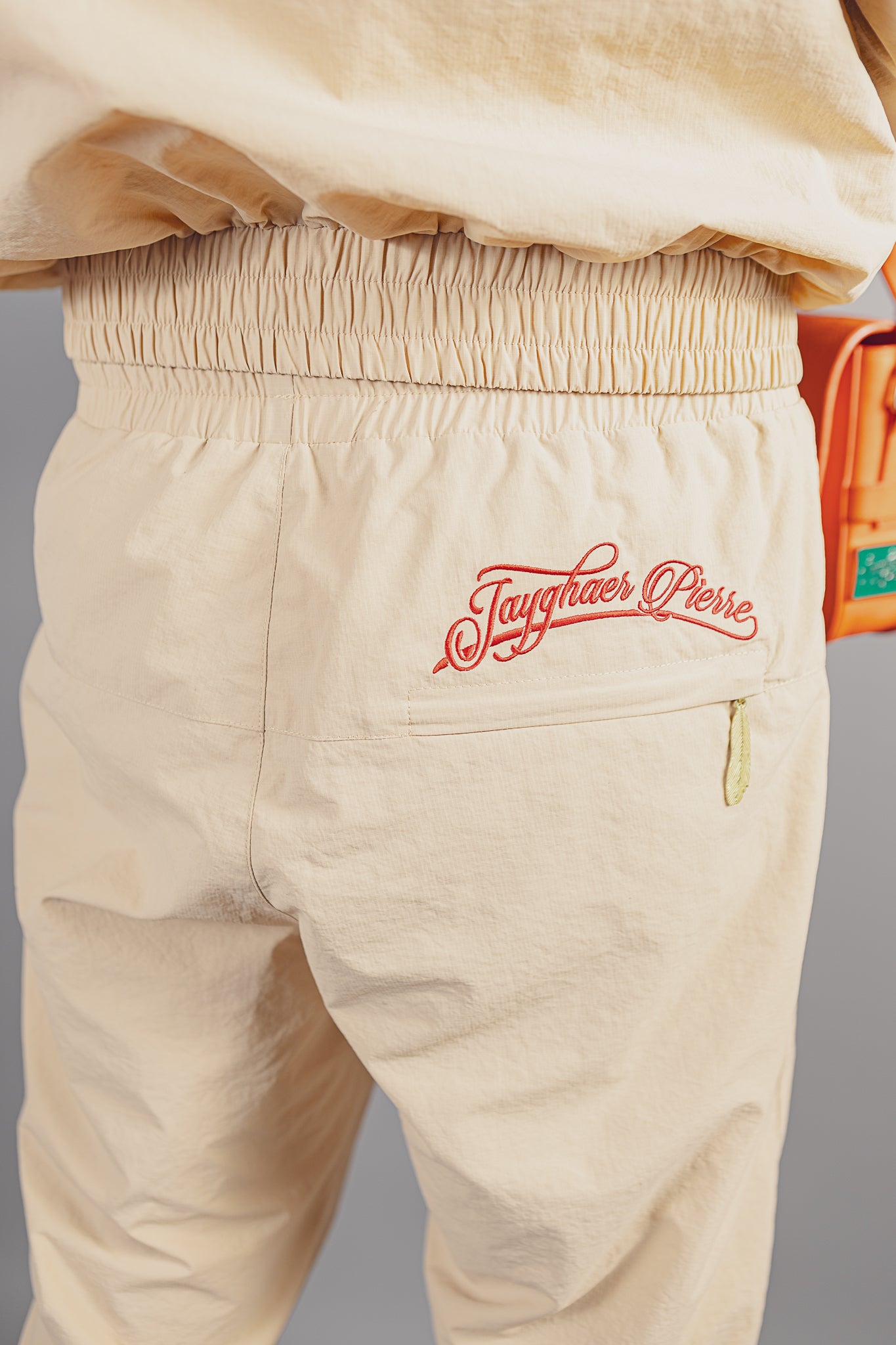 Beige luxury pants with elastic waistband and red Jayghaer Pierre branding on back pocket